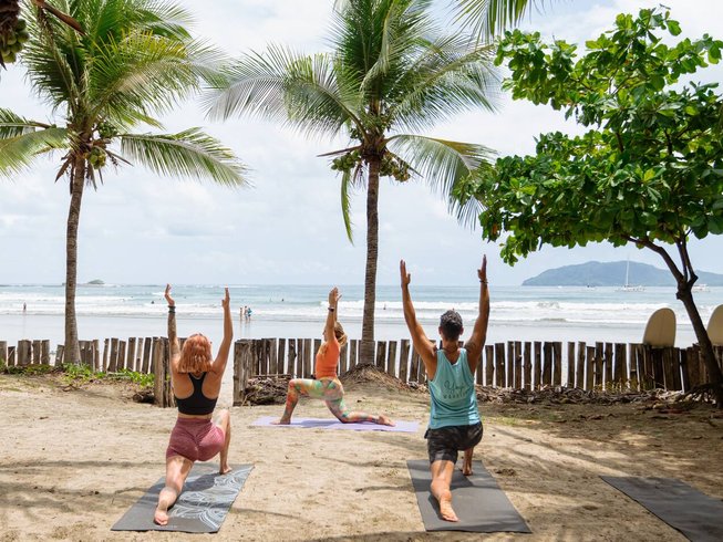 Small group practicing yoga on the beach near Tamarindo Costa Rica with palm trees and ocean views.